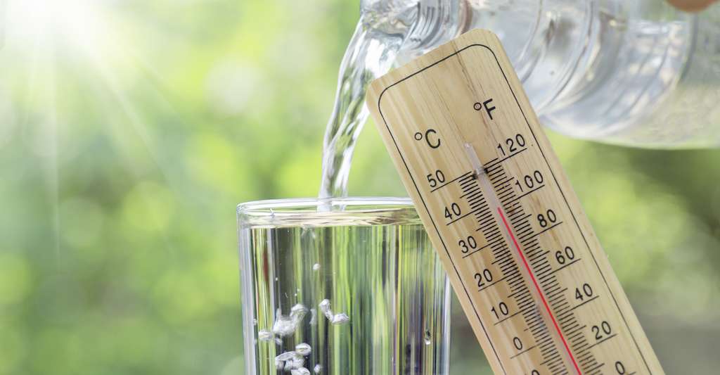 Verre d’eau rempli à côté d’un thermomètre sous le soleil